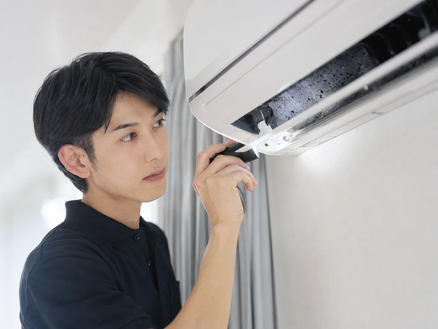 エアコン吹き出し口の黒い点や汚れをライトで確認するスタッフ